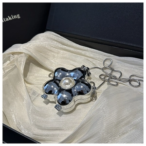 Detalle de mini bolso plateado en forma de flor con perla central y cadena de serpiente