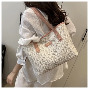 Detail of hollow woven straw tote bag with pink leather handles and gold rivet accents