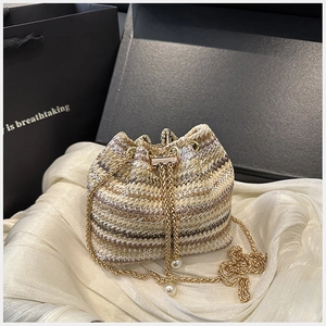Detail of woven bucket bag with gold chain strap and pearl charm on silk fabric