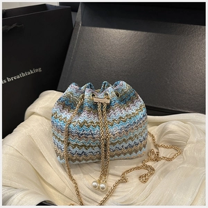 Close-up of zigzag woven bucket bag featuring pearl charms and a golden chain strap