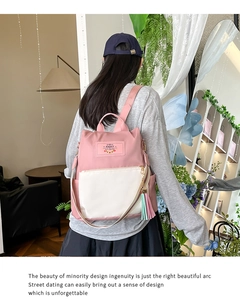 Detail view of the pink and beige nylon backpack with a decorative tassel and logo