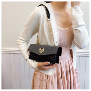 Detail of black crossbody bag with gold M logo and chain strap worn by model