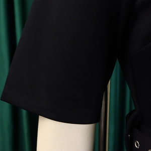 Close-up of short sleeve cuff and metal eyelet belt detail on black V-neck A-line dress