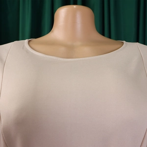 Detailed close-up of the elegant round neckline and premium knit fabric on a beige dress