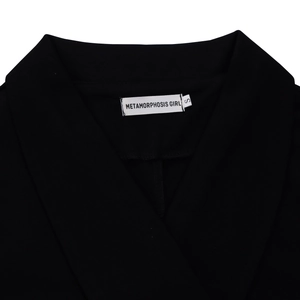 Detailopname van de V-hals en het witte merklabel op een zwart blazerpak voor dames