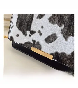 Gros plan du sac à bandoulière imprimé vache avec boucle dorée et détail de bandoulière