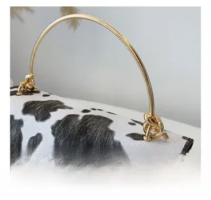 Détail d'un sac à main imprimé vache montrant la poignée dorée et les finitions chic