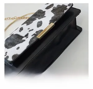 Gros plan des coutures d'un sac en cuir imprimé vache avec bandoulière chaîne dorée