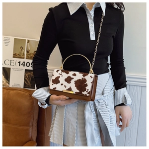 Détail du sac à motif vache avec poignée ronde dorée et bandoulière chaîne sur modèle