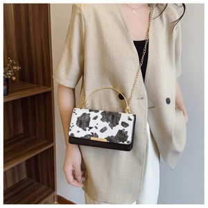 Detalle del bolso con estampado de vaca, asa de metal dorado y correa de cadena