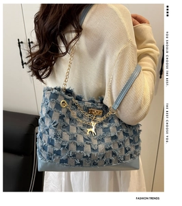 Detail of blue denim bucket bag with fringe edges, gold chain, and deer pendant