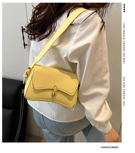 Close-up of bright yellow crossbody bag with gold buckle on white shirt background