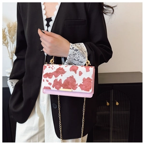 Sac bandoulière rose à motif vache et poignée dorée porté par un mannequin en tenue chic