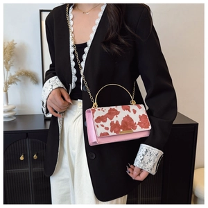 Detalle del bolso rosa con estampado de vaca y asa metálica dorada con cadena