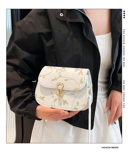 Gros plan du sac beige avec broderie florale délicate et boucle fer à cheval dorée