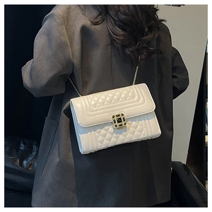 Detail of quilted leather crossbody bag with gold chain strap on a grey blazer