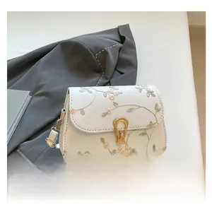 Détail de la broderie en dentelle florale et boucle dorée sur le sac de selle blanc