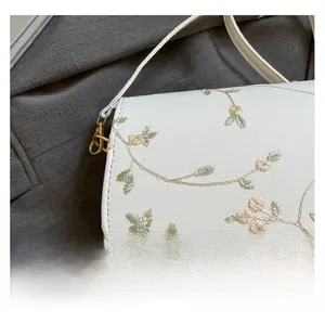 Détail d'un sac selle en tissu blanc avec broderies de feuilles vertes et fleurs roses
