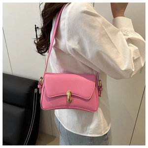 Detailed view of a pink flap shoulder bag with a gold metal clasp worn by a model