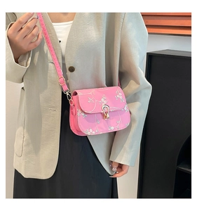 Gros plan du sac besace rose avec broderie florale blanche et boucle en métal doré