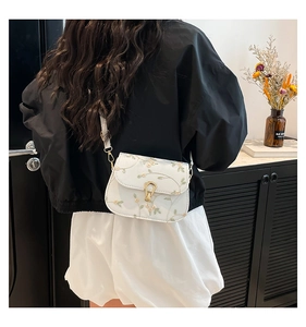 Dettaglio del ricamo floreale su una borsa a sella bianca indossata da una modella in stile rétro