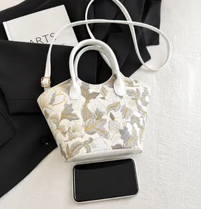 Detail view of floral embroidery on a chic cream bucket bag with white leather handle