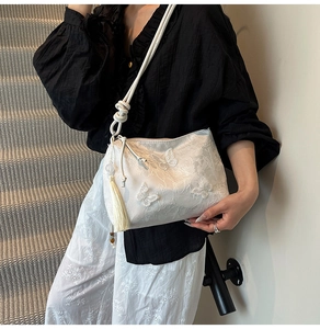 Detail of white lace embroidery and butterfly accents on a stylish crossbody bucket bag