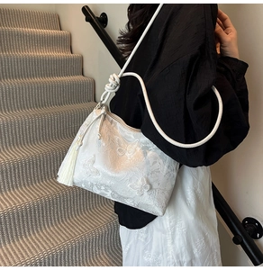 Close-up of white lace shoulder bag featuring 3D butterfly embroidery and fringe tassel