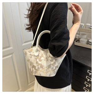 Detailed embroidery of yellow floral patterns on a white tote bag with leather strap