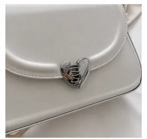 Detailansicht der weißen Ledertasche mit silbernem Herz-Metallverschluss und Textur