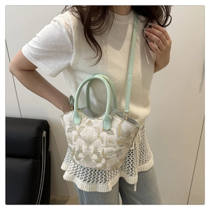 Detail of floral embroidery on a light green bucket bag with adjustable shoulder strap