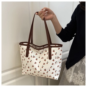 Chic tote bag with red cherry prints and brown straps held by a model in casual attire