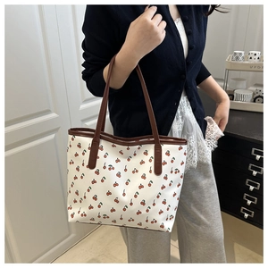 Detail of white tote bag with red cherry print and brown leather handles on shoulder