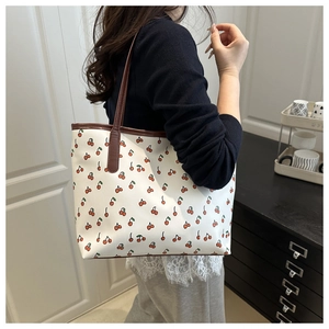 Detail of cute cherry print tote bag with brown leather handles worn by a model