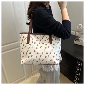 Detailed view of tote bag with cherry print and brown handles worn by a model