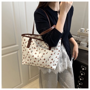 Detail of a white tote bag featuring red cherry prints and brown leather straps