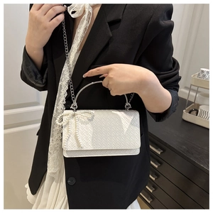 Close-up of woven shoulder bag with pearl bow detail and silver chain strap