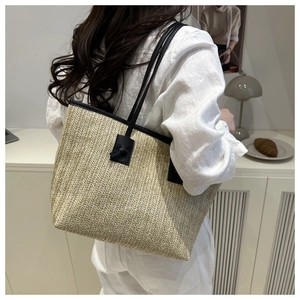 Gros plan sur un grand sac cabas en paille avec lanières en cuir noir et détail de nœud