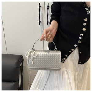 Detalle de bolso trenzado plateado con lazo de perlas y asa de metal circular