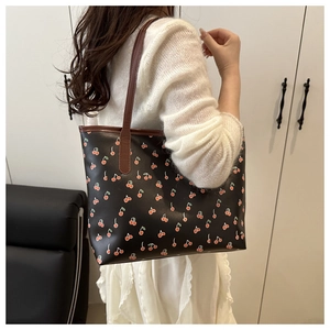 Close-up of cute cherry print pattern on black tote bag with brown leather shoulder strap