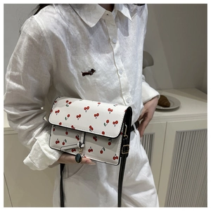 Dettaglio di una borsa a tracolla bianca con stampa ciliegie rosse e tracolla nera donna