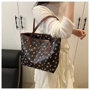 Detail of shoulder tote bag featuring cherry print and brown handles on a female model