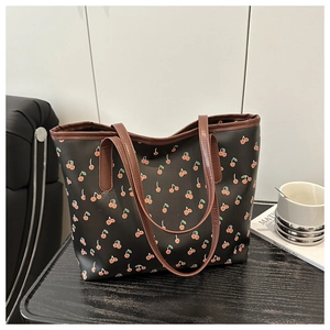 Detail of a black tote bag with cherry prints and brown leather handles on a dark table