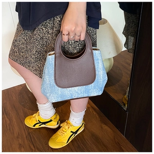 Detail van lichtblauwe denim handtas met zilveren klinknagels en bruin lederen handvat