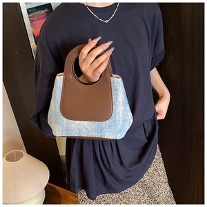 Detail van de ringgreep op de tweekleurige bucket bag van denim en bruin leer