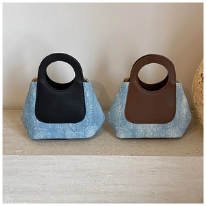 Detail van twee mini denim emmertassen met contrasterende lederen hengsels op steen