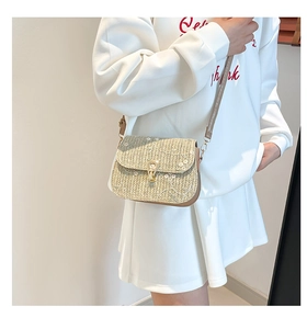 Détail du sac selle en paille avec broderie florale blanche et fermoir rotatif doré