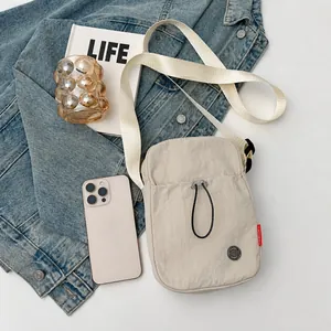 Détail d'un sac bandoulière en nylon beige avec cordon de serrage et sangle blanche