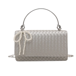 Silver woven shoulder bag with round metal handle and pearl bow charm on white background