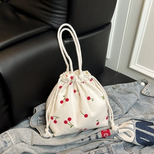 Detail der weißen Cord-Beuteltasche mit roten Kirschstickereien auf Denim-Hintergrund